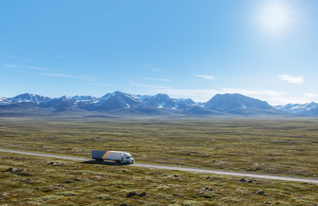 A single semi truck on a road crossing open tundra toward a distant mountain range