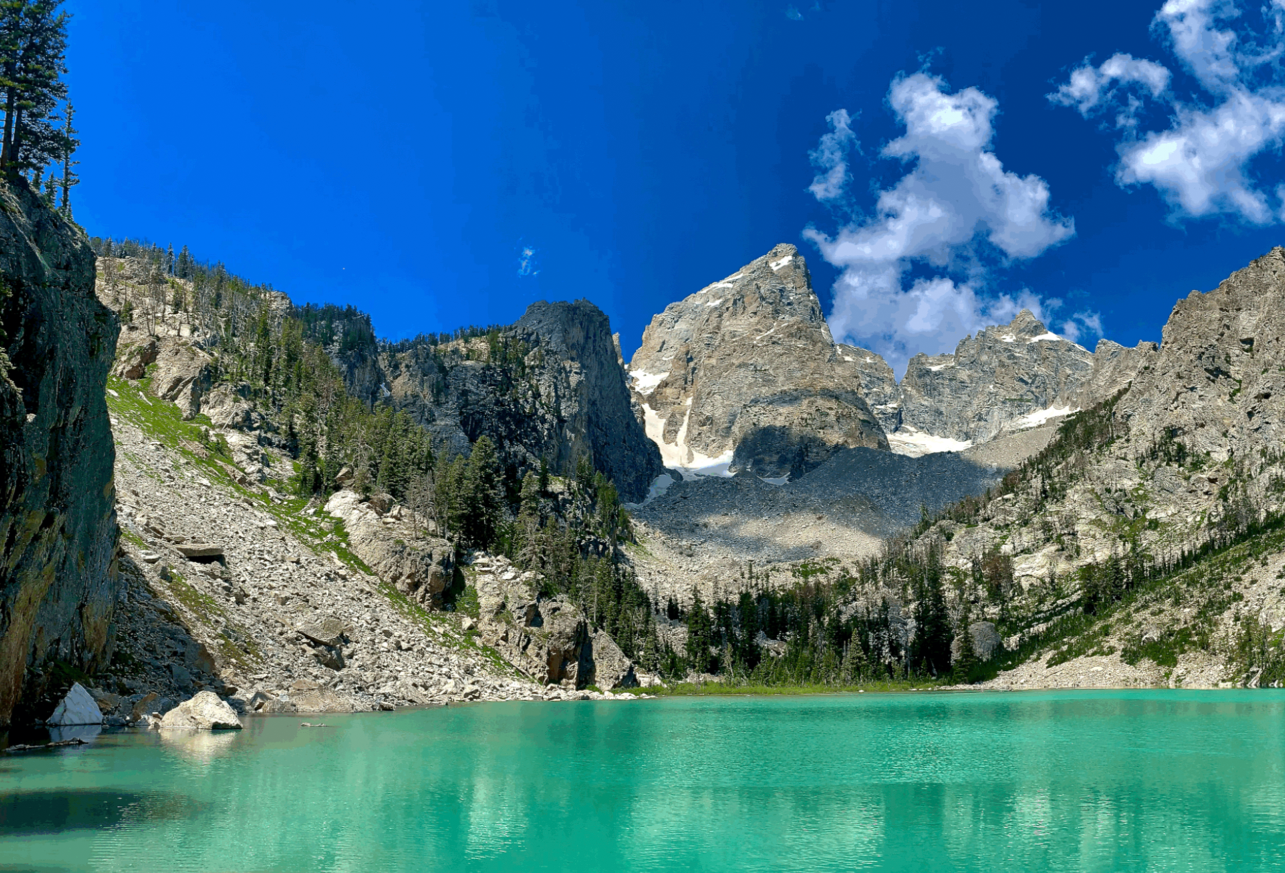 A turquoise alpine lake beneath granite Teton peaks under a clear blue sky